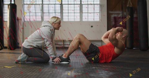 Female trainer assisting male client performing situps with fitness data overlays in gym