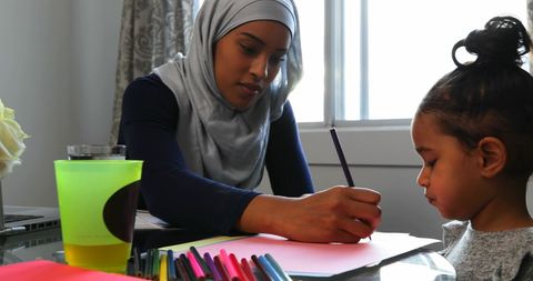 Mother in Hijab Assisting Daughter with Drawing at Home