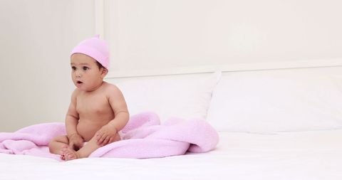 Adorable Baby Wearing Pink Cap Sitting on Bed