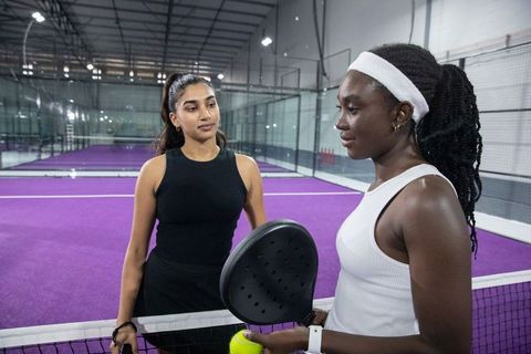 Two women practicing padel on purple court holding racket and ball in indoor sports arena