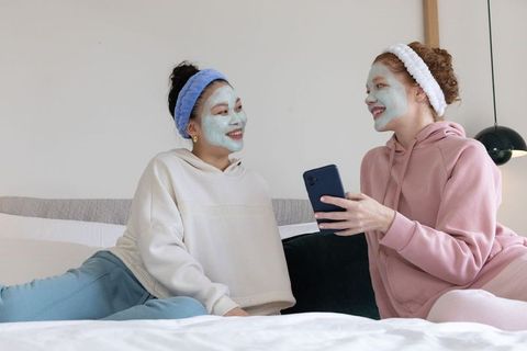 Diverse friends having at-home spa night with mint face masks, terry headbands, cozy loungewear