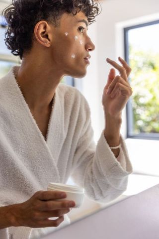Man Applying Moisturizer While Wearing White Bathrobe in Bright Bathroom