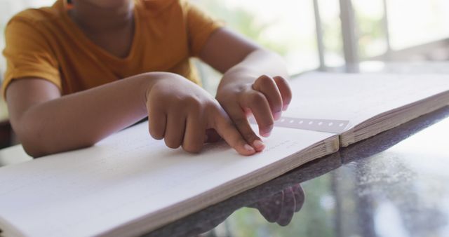 Young child reading Braille alphabet on notebook with fingers. Ideal for use in educational and awareness materials for visually impaired individuals, articles on inclusive education, and campaigns promoting literacy for people with disabilities.