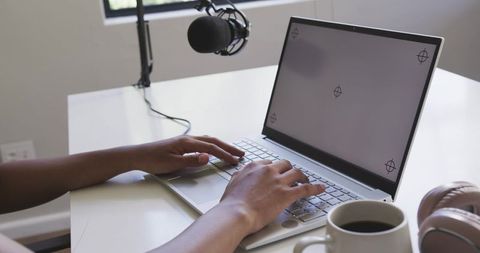 African american woman typing on laptop recording podcast with boom microphone in studio