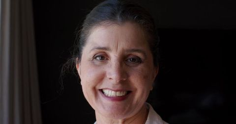 Smiling mature woman in warm natural light wearing collared blouse, elegant headshot