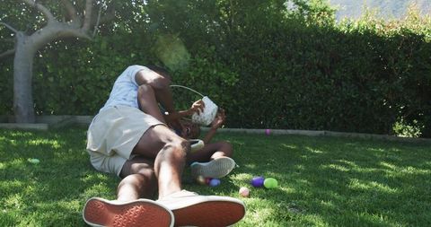 African american father and son wrestling and playing on lawn with easter eggs and basket