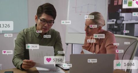 Coworkers reviewing social media engagement metrics on laptop and printed reports