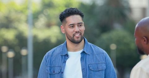 Multicultural men chatting on tree-lined street wearing denim shirt casual urban friendship