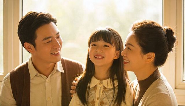 Smiling parents embracing daughter by sunlit window, warm cozy family moment at home