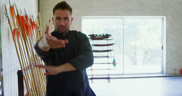 A man practicing martial arts in a training hall. He appears focused and dedicated, performing precise movements. The background includes traditional martial arts weapons displayed on racks. Ideal for use in content related to fitness, martial arts training, self-discipline, and traditional combat techniques.
