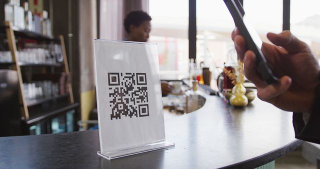 Hand of customer using smartphone to read qr code on the bar at a cafe. service technology at a small independent cafe business.