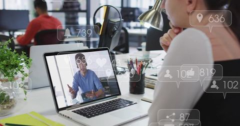 Remote presenter engaging team on laptop in open-plan office with social media overlays