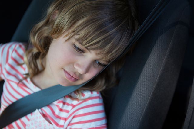 Teenage girl sitting in the back seat of a car, wearing a seatbelt and looking thoughtful. Ideal for use in articles about child safety, travel, family journeys, or emotional moments during travel.