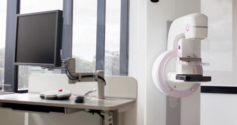 Mammography machine in bright clinic exam room with monitor, paddle, detector