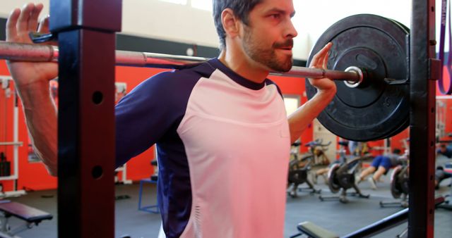 Man lifting barbell while performing squat in gym. Can be used for fitness blogs, workout tutorials, gym advertisements, strength training programs.