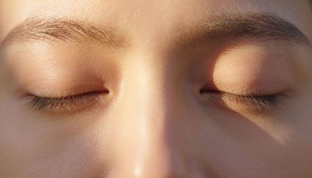 Resting woman showing closed eyelids, natural eyebrow hairs and skin texture closeup