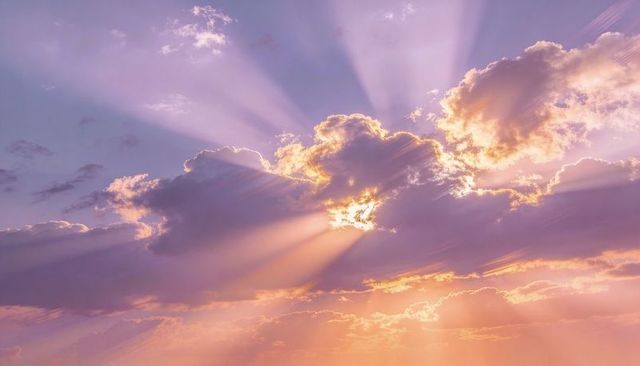 Backlit cumulus clouds casting golden sunbeams over pastel peach sky at sunset