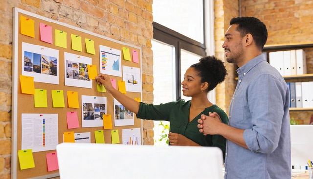 Collaborating on creative project using colorful sticky notes on corkboard in modern office