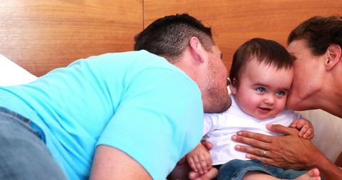 Parents Kissing Happy Baby in Bedroom