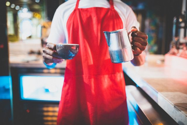 African american male barista holding a cup and a pot looking at camera. independent small business owner.