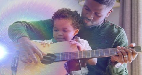 Father teaching baby to play acoustic guitar while sharing tender musical bonding moment