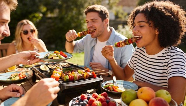 Young friends enjoying backyard barbecue with colorful kebab skewers and portable grill