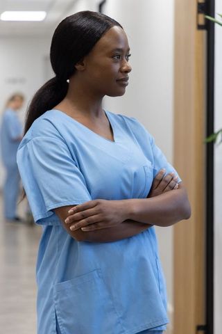 Confident african nurse standing with crossed arms in modern clinic corridor, composed