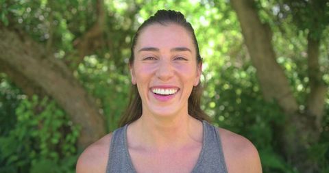 Smiling young woman enjoying sunny park wearing grey athletic tank top, healthy lifestyle portrait