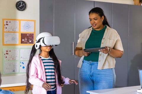 Teacher guiding asian student using virtual reality headset in diverse classroom learning