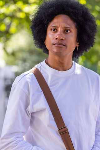 African-american man gazing upward in sunlit park wearing white shirt and messenger bag