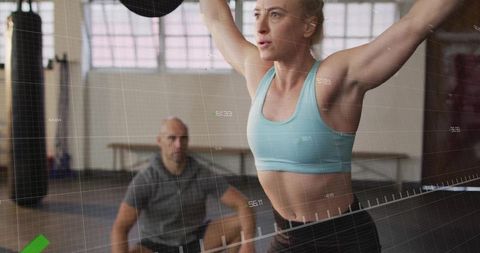 Female Athlete Lifting Medicine Ball in Gym with Trainer's Guidance
