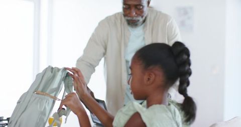 Mature man helping young girl adjust backpack straps at table for school morning routine