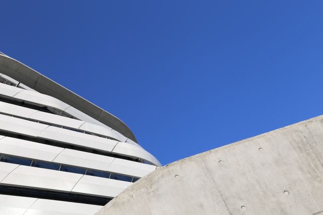 Modern architectural structure captured against a clear blue sky, showcasing clean lines and contemporary design elements. The image is ideal for projects related to urban development, architectural design, or real estate. It emphasizes minimalism and modernity, suitable for marketing materials, website backgrounds, or editorials focused on contemporary architecture.