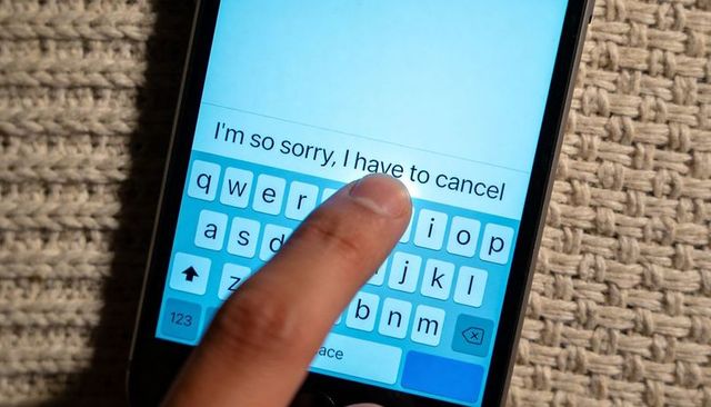 Finger tapping smartphone keyboard composing apology message 'i am so sorry, i have to cancel'