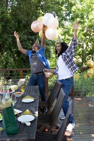Diverse male friends celebrating outdoors with balloons and party hats