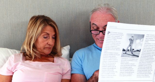 Serious senior couple on bed reading newspaper and book in bedroom