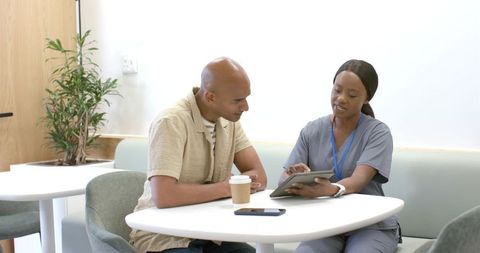 African american nurse consulting patient in clinic lounge using tablet
