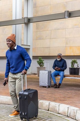 Young african american man walking with suitcase while senior man sitting and waiting