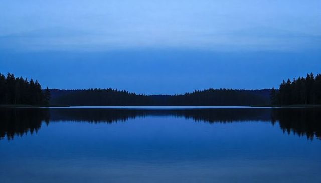 Blue twilight lake reflection mirroring forest silhouette on glassy still water at dusk