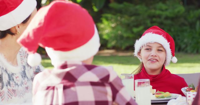 Family members wearing Santa hats, sharing laughter and enjoying a festive meal outside. Perfect for holiday greeting cards, family event promotions, and festive advertisements highlighting joyful family gatherings during Christmas time.