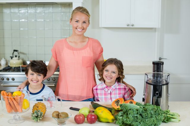 Mother and two children standing in kitchen surrounded by fresh fruits and vegetables. They are smiling and appear to be preparing healthy food together. Ideal for use in articles about family bonding, healthy eating, parenting, and lifestyle.