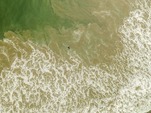 Aerial View of Ocean Waves and Lone Surfer Amidst Swirling Foam