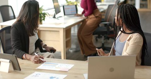 Diverse female team collaborating over analytics charts and laptops in modern office