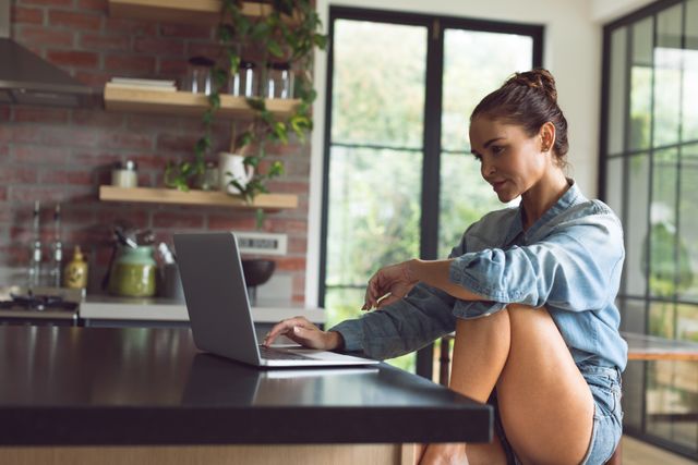 Beautiful woman using laptop on worktop in kitchen at comfortable home
