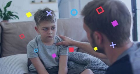 Father consoling upset son on sofa with comforting hand on shoulder and colorful graphic overlays