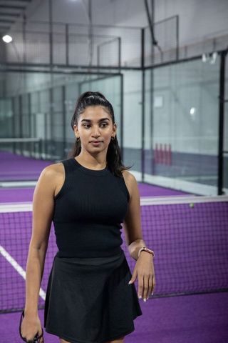 Indian female tennis player standing at net on purple indoor court wearing smartwatch