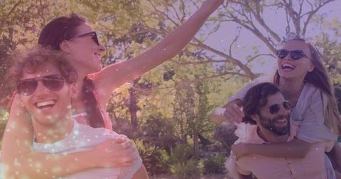 Friends enjoying piggyback rides in sunlit park with sparkling light overlay, summer fun