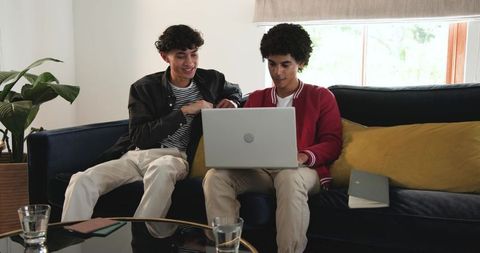 Young men collaborating on laptop on living room couch, casual remote work and study