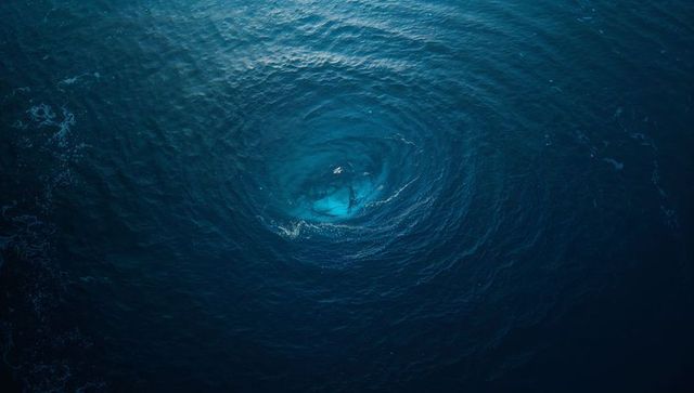 Aerial Whirlpool Spiraling Over Deep Ocean with Turquoise Core and Concentric Ripples