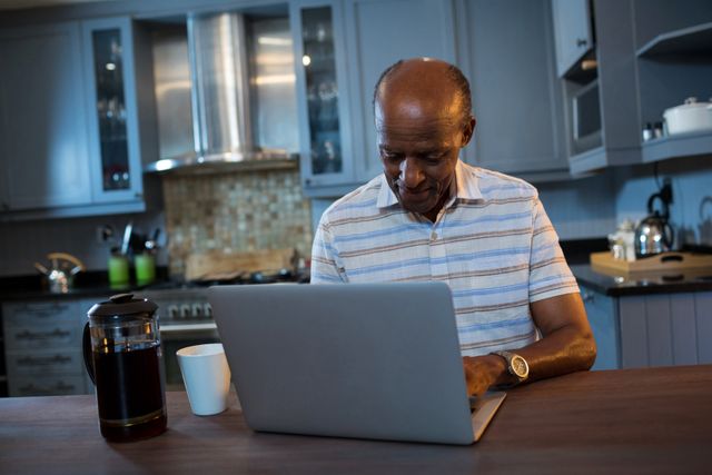 Senior man using laptop at table in kitchen at home